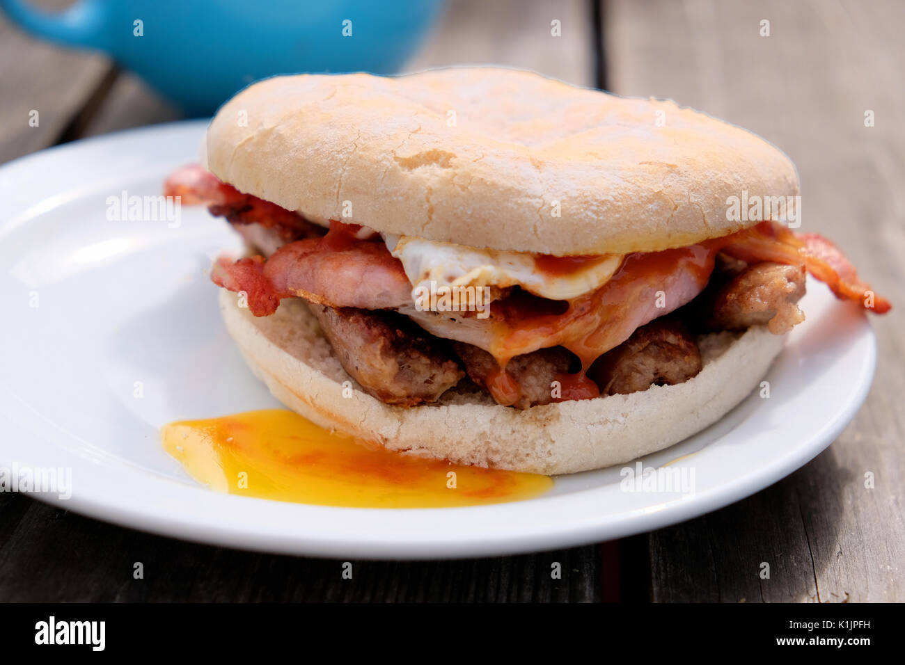 Una fresca colazione cucinata bap. Bacon, salsicce e uova fritte cotte a un outdoor cafe e servita in un panino. Foto Stock