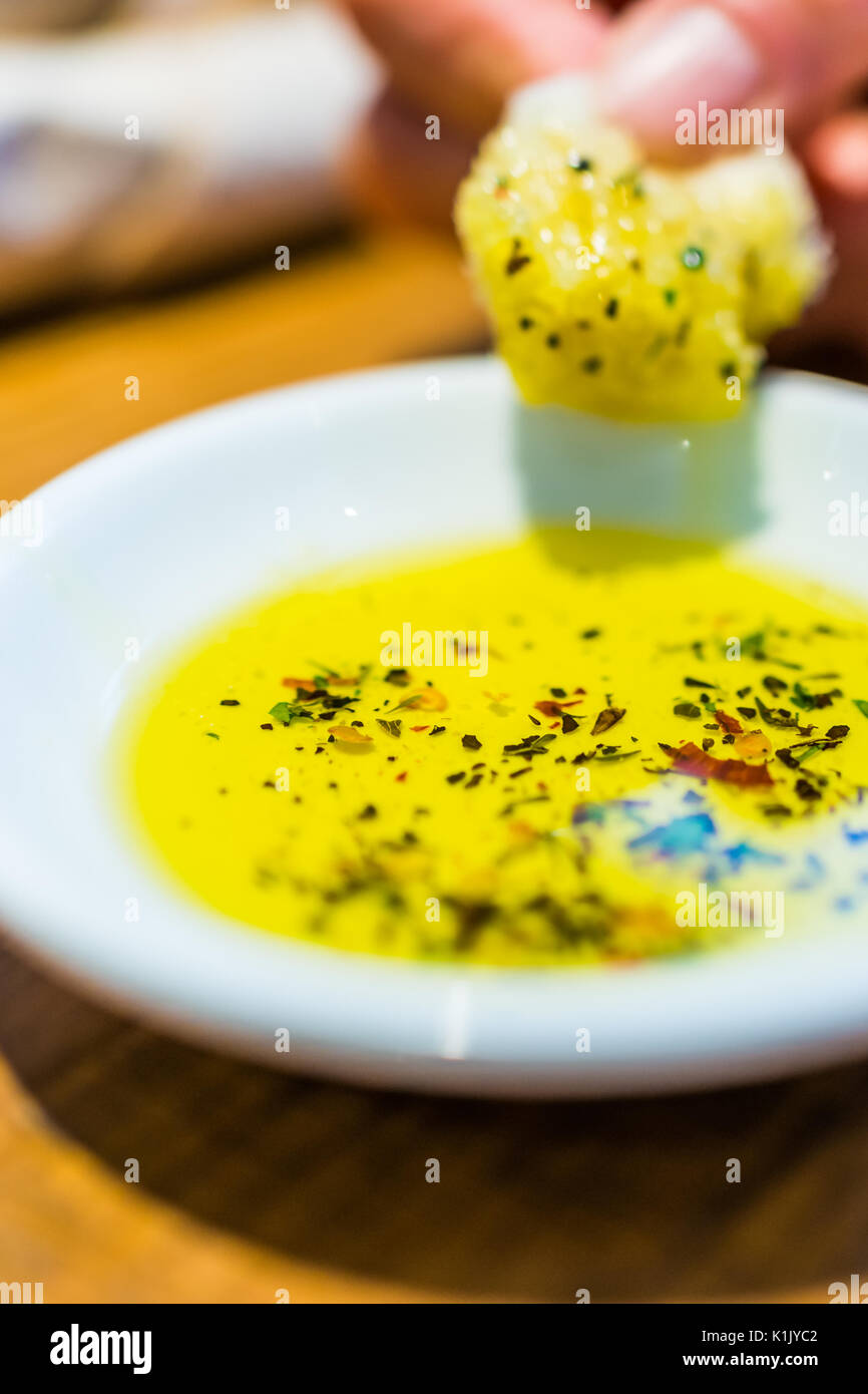 Persona di immersione a mano fetta di pane in erborinati olio d'oliva in ristorante Foto Stock