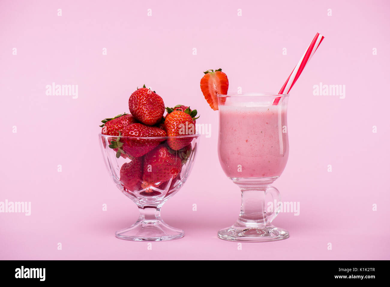 Delizioso frullato fragole in vetro con paglia e fragole fresche in un recipiente isolato in rosa Foto Stock