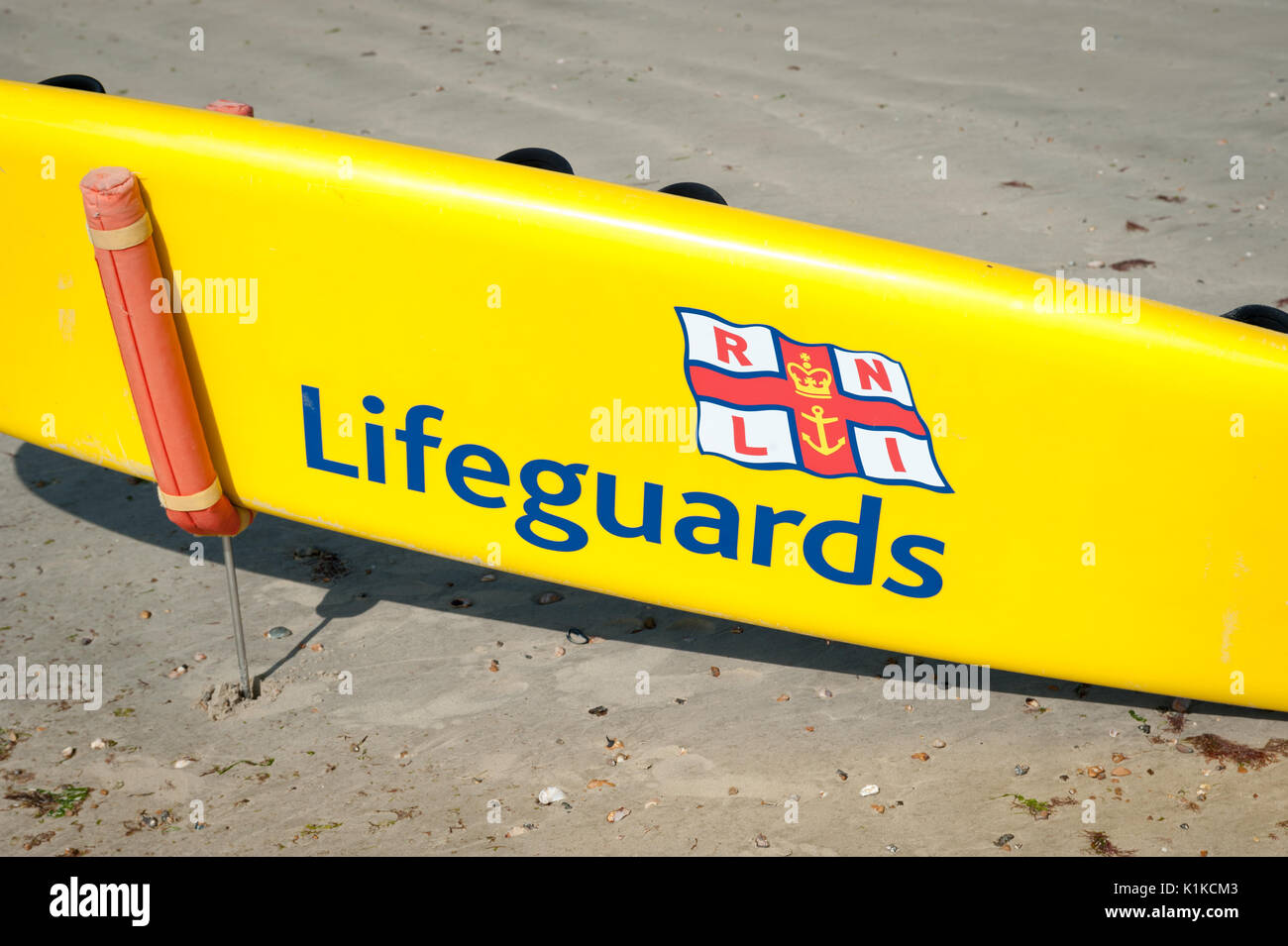 Un giallo bagnino RNLI paddle board su una spiaggia di sabbia durante la bassa marea su una giornata d'estate in Littlehampton West Sussex, in Inghilterra. Foto Stock