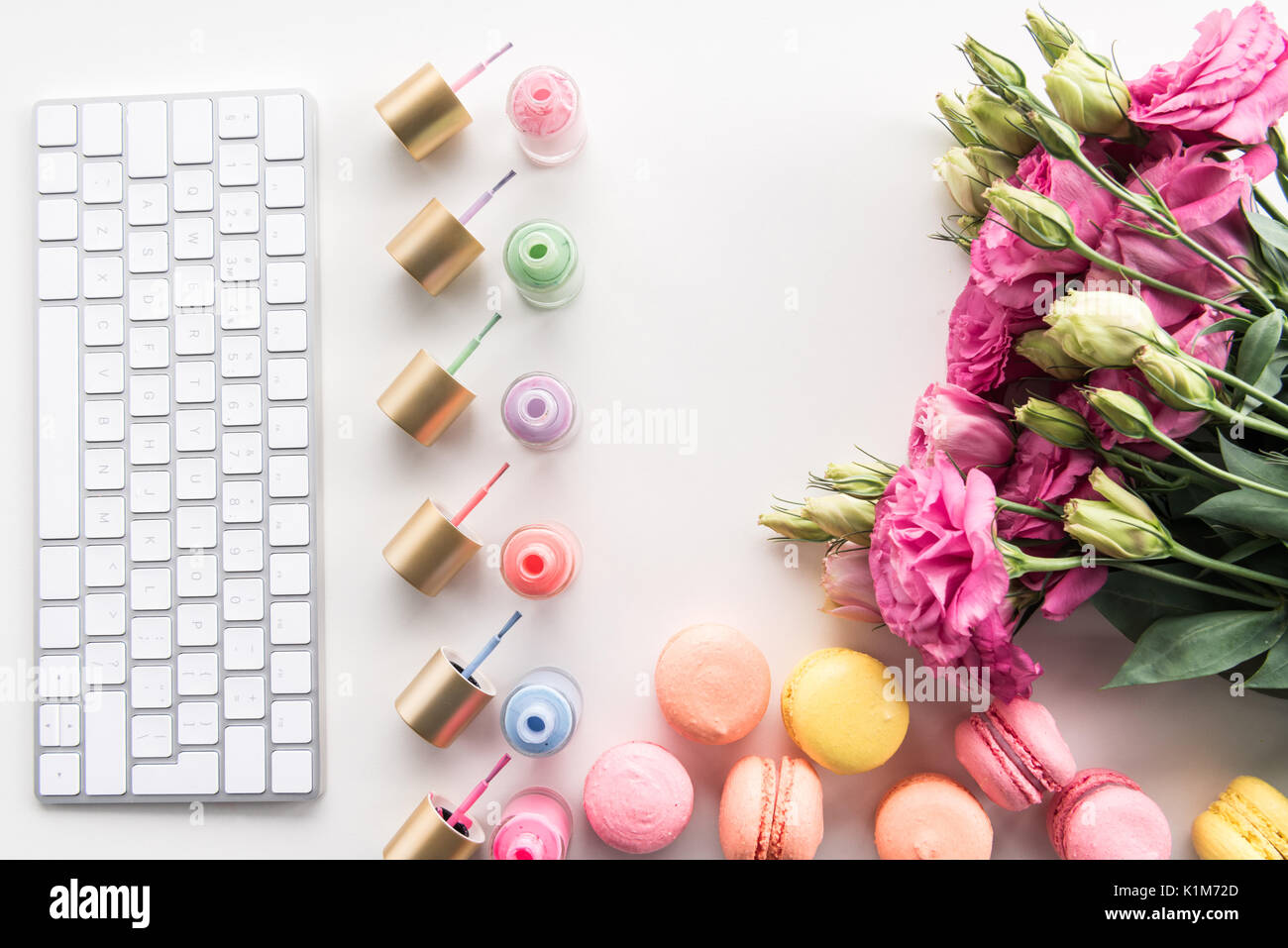 Lay piatto con tastiera e colorati di smalti per unghie, macarons e fiori isolati su bianco Foto Stock