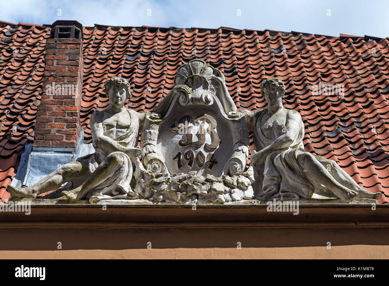 Art Nouveau figure su un tetto con le iniziali del costruttore, Lubecca, Schleswig-Holstein, Germania Foto Stock