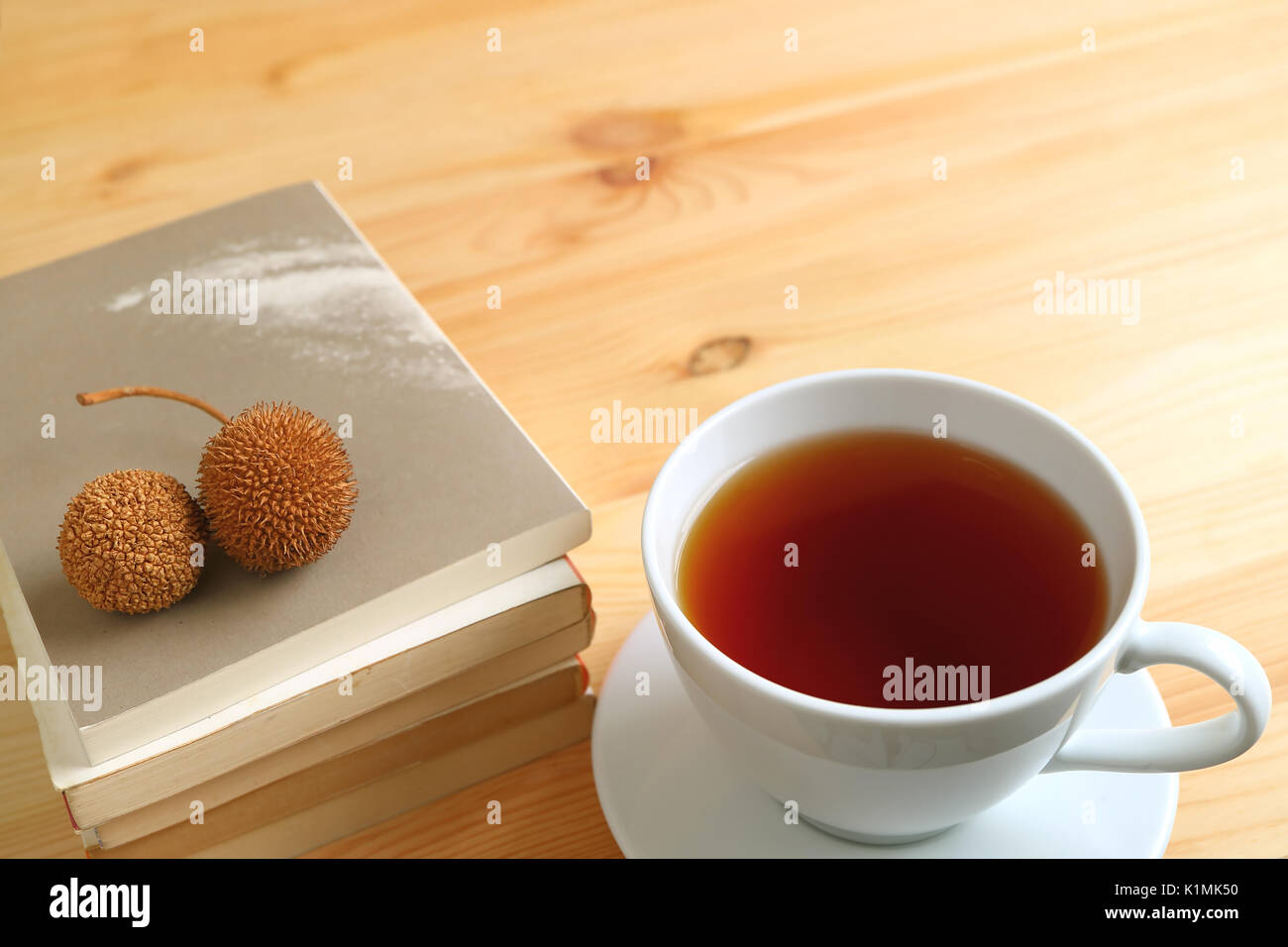 Una tazza di tè caldo con una coppia di secco coni di pino sulla pila di libri sul colore naturale tavolo in legno Foto Stock