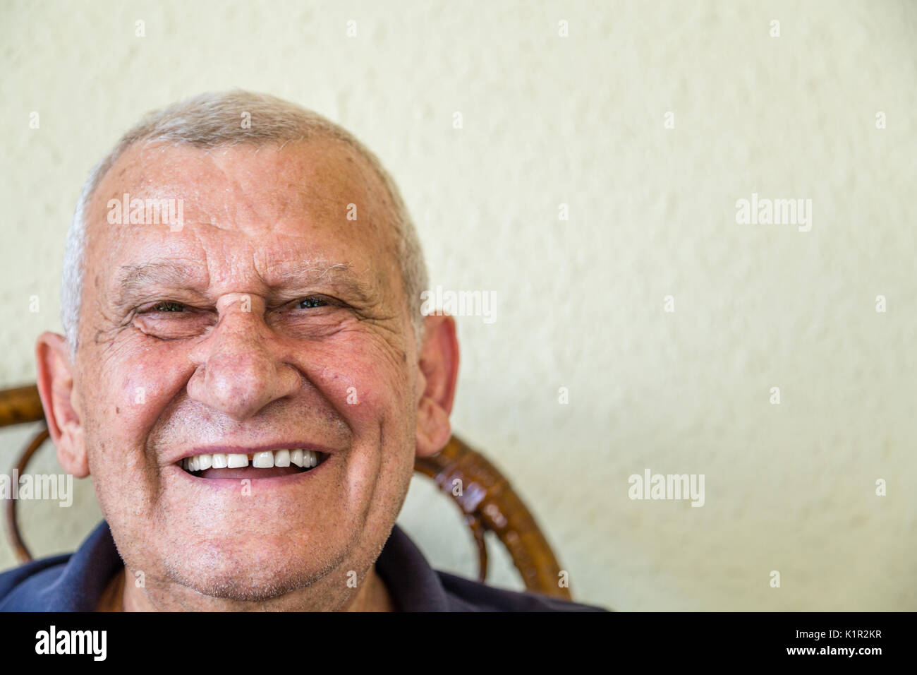 Il vecchio uomo sorridente mentre è seduto sulla sedia di vimini Foto Stock