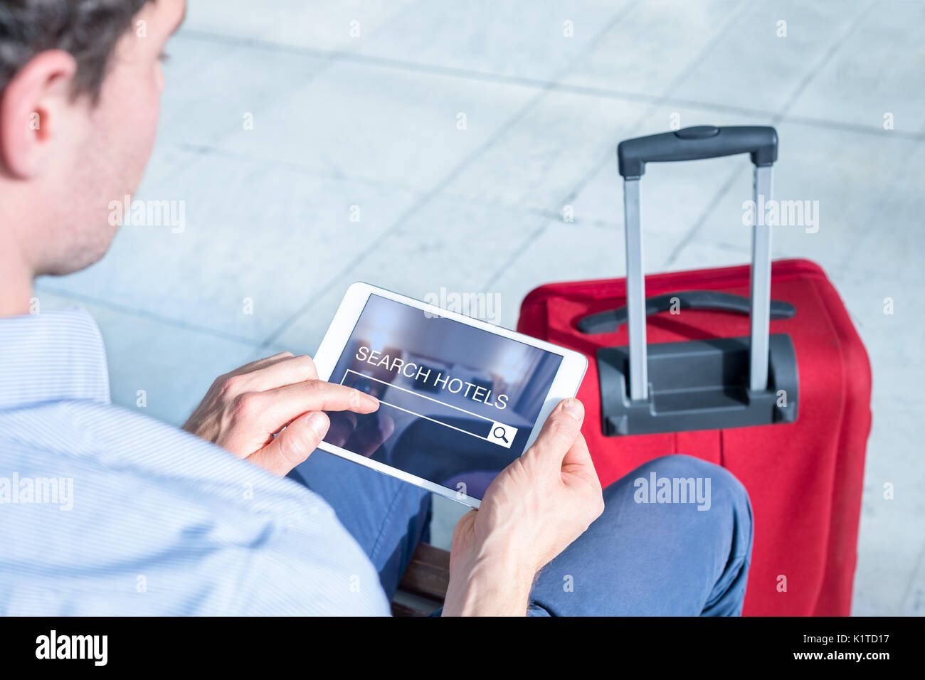 Imprenditore utilizzando una tavoletta digitale computer per cercare e prenotare hotel camera con sito web online, terminale di un aeroporto interno Foto Stock