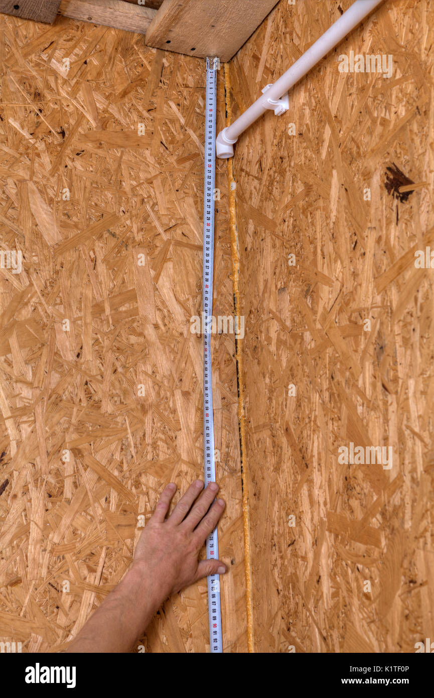 Plumber installazione tubi in casa, la misurazione della distanza su di una parete di legno utilizzando un nastro di misurazione, montaggio a parete in plastica della tubazione dell'acqua. Foto Stock