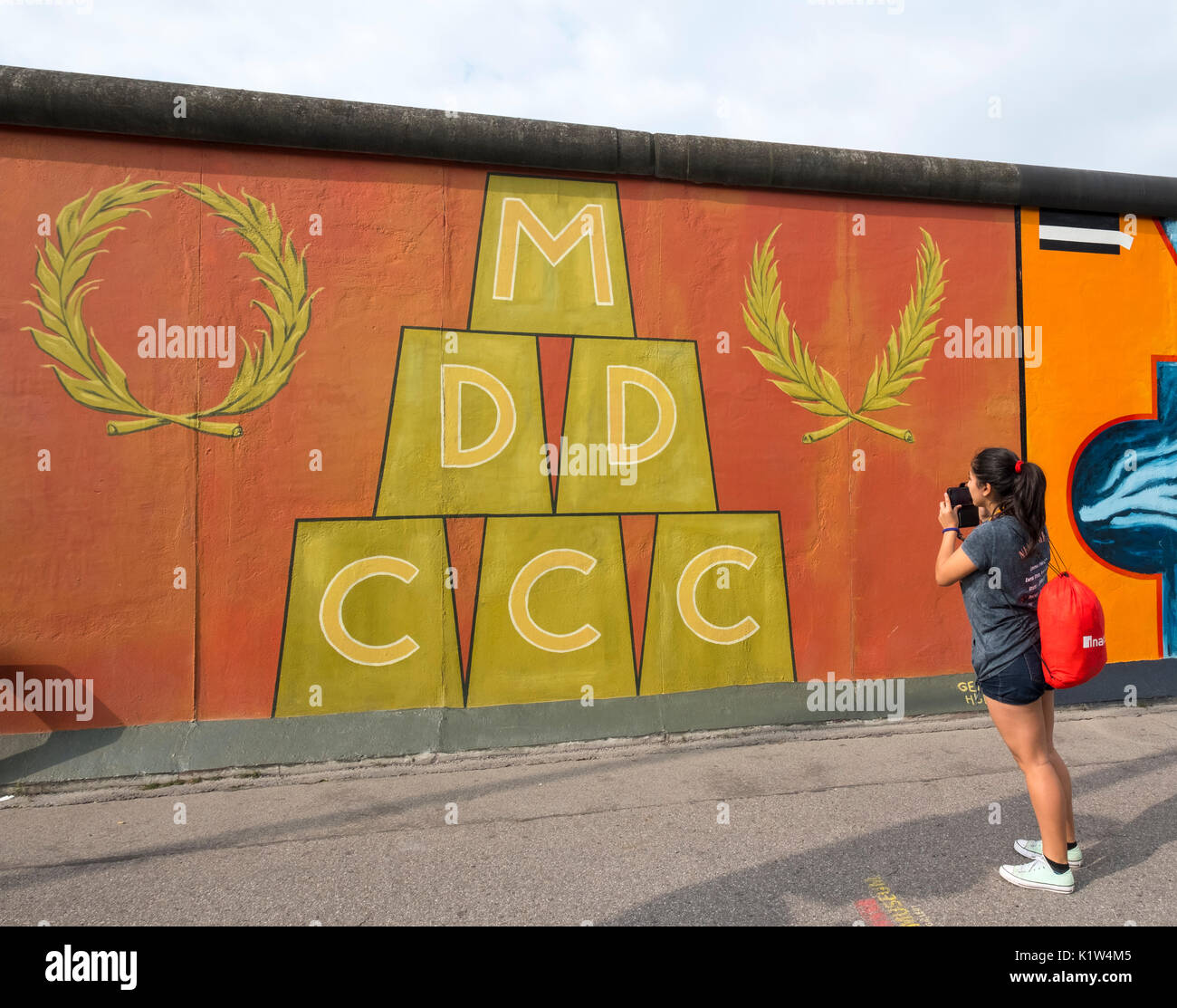 Turistica prendendo fotografia del murale dipinto sulla sezione originale del muro di Berlino a East Side Gallery di Berlino, Germania Foto Stock