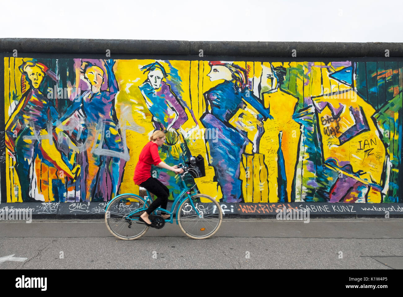 Ciclista passa su un murale dipinto sulla sezione originale del muro di Berlino a East Side Gallery di Berlino, Germania Foto Stock