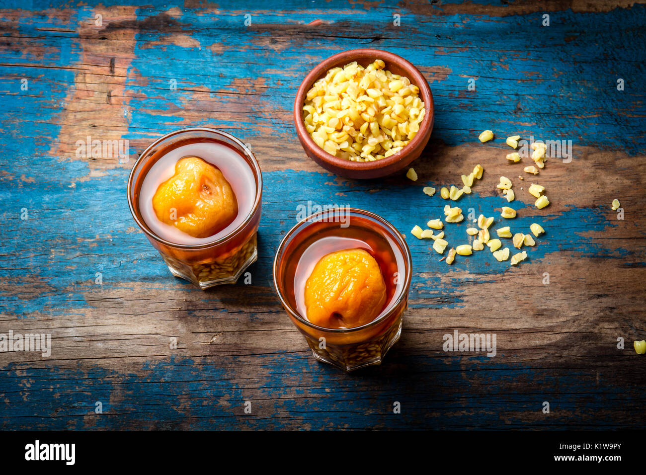 Mote con huesillo. Tradizionale bevanda cilena realizzato da cuocere il riso semigreggio e grano essiccato peach sulla tavola di legno, rustico sfondo blu. Foto Stock