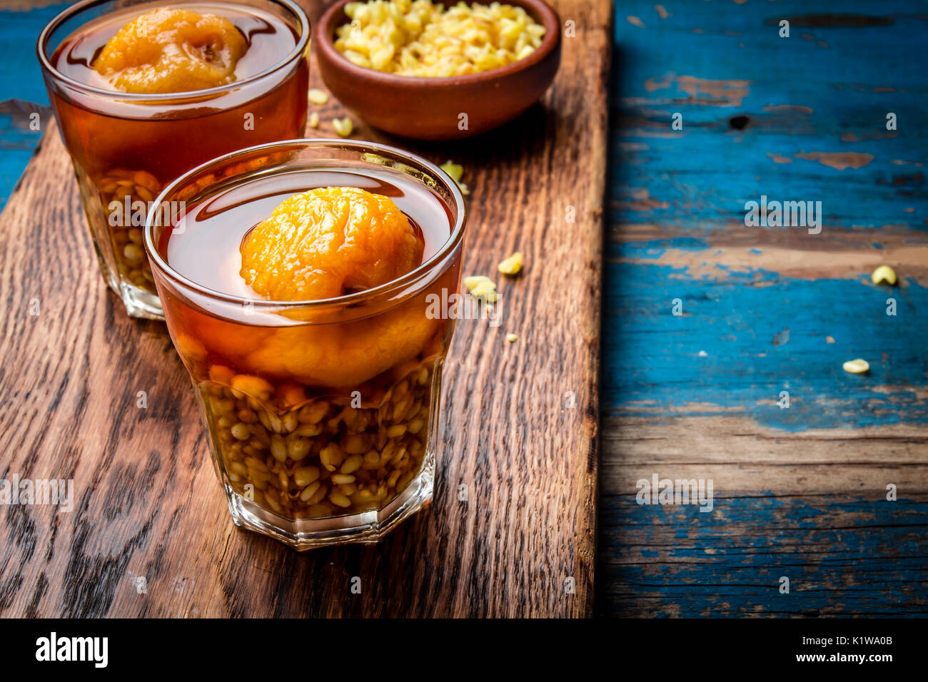 Mote con huesillo. Tradizionale bevanda cilena realizzato da cuocere il riso semigreggio e grano essiccato peach sulla tavola di legno, rustico sfondo blu. Foto Stock