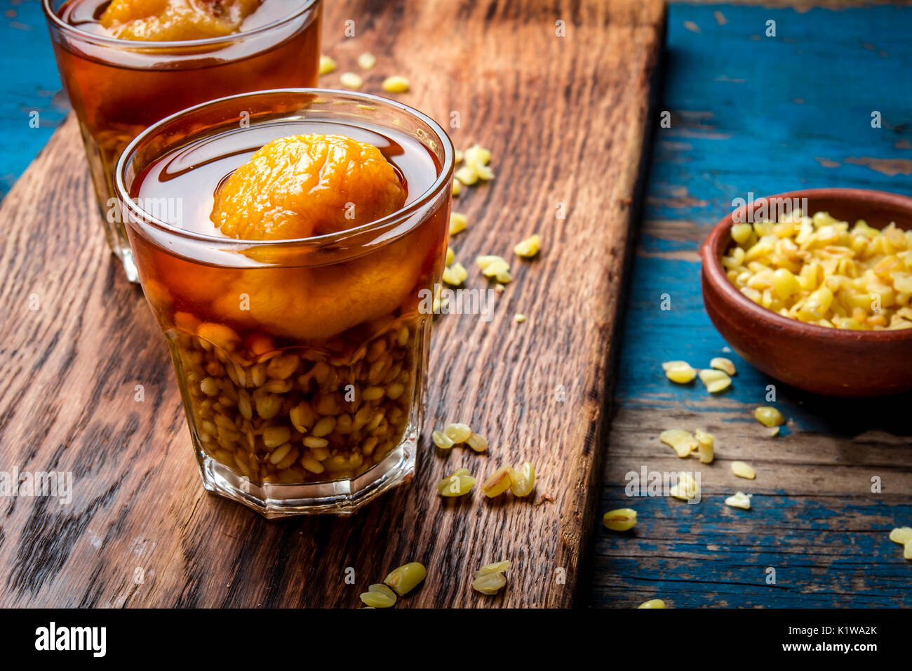 Mote con huesillo. Tradizionale bevanda cilena realizzato da cuocere il riso semigreggio e grano essiccato peach sulla tavola di legno, rustico sfondo blu. Foto Stock
