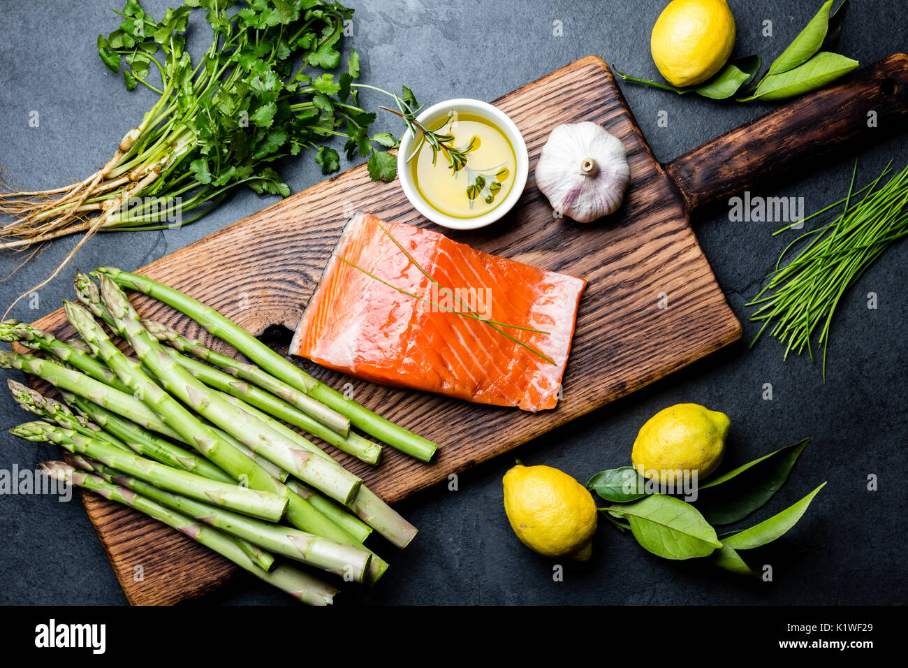 Ingredienti per la cottura. Materie filetto di salmone, gli asparagi e le erbe sul pannello di legno. Per la cottura di alimenti con sfondo spazio copia. Vista superiore Foto Stock