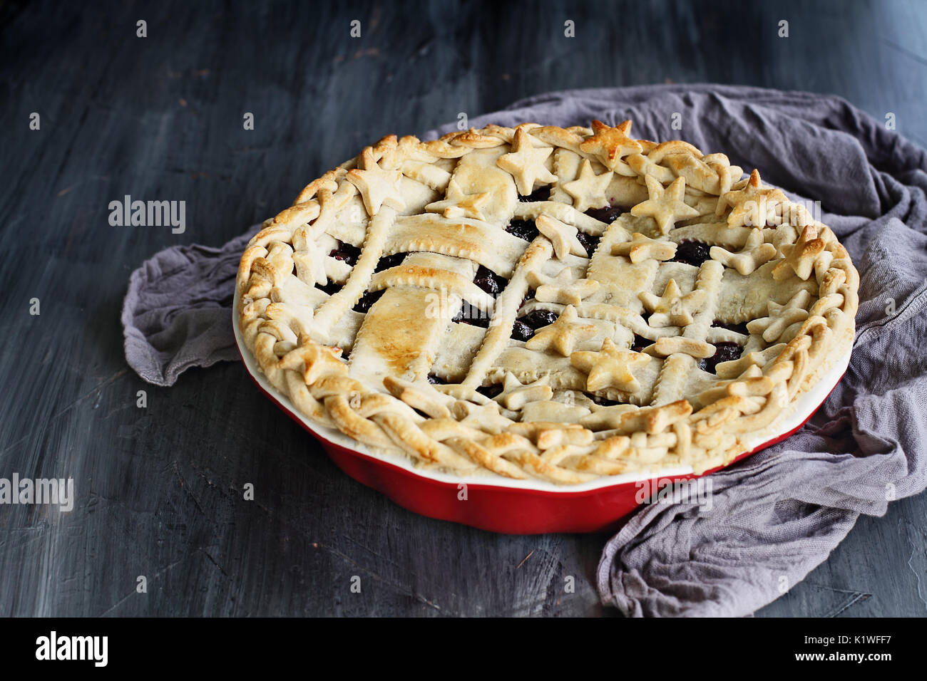 Dolce torta ai mirtilli con reticolo e stelle crosta in un grafico a torta rossa piastra contro un rustico sfondo di legno. Foto Stock