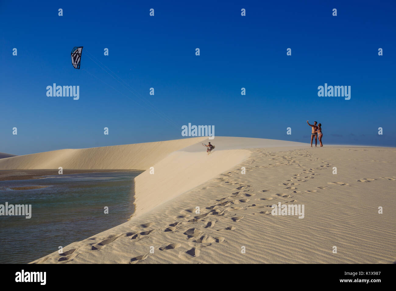 Torists prendendo un selfie mentre un kite-surfer è in procinto di Kitesurf in una pioggia naturale piscina tra le dune di Jericoacoara, Ceará, Brasil Foto Stock
