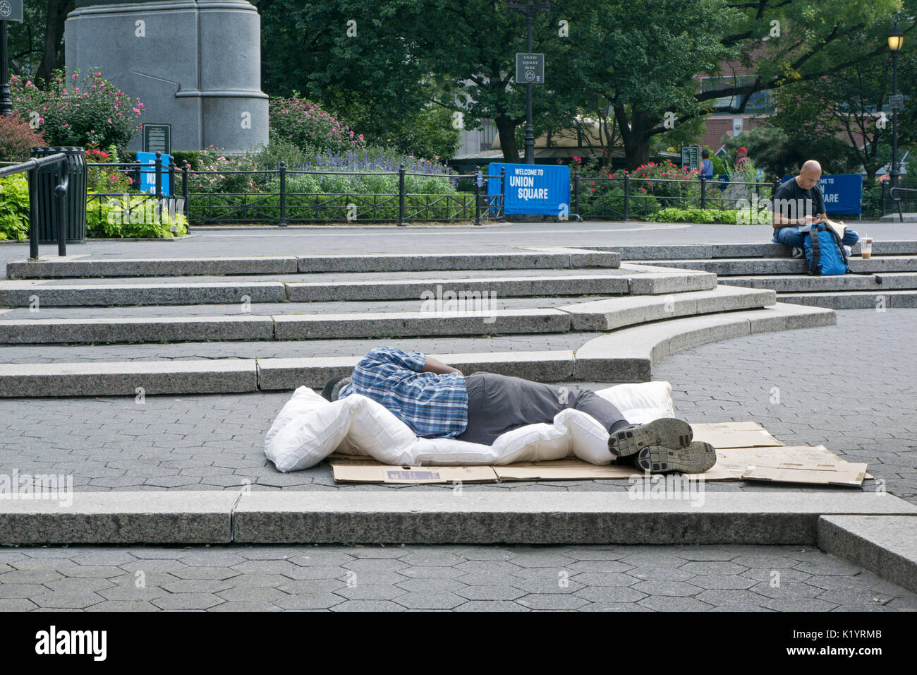 Un uomo non identificato, presumibilmente senzatetto, dormire durante la tarda mattinata in Union Square Park a Manhattan, New York City Foto Stock