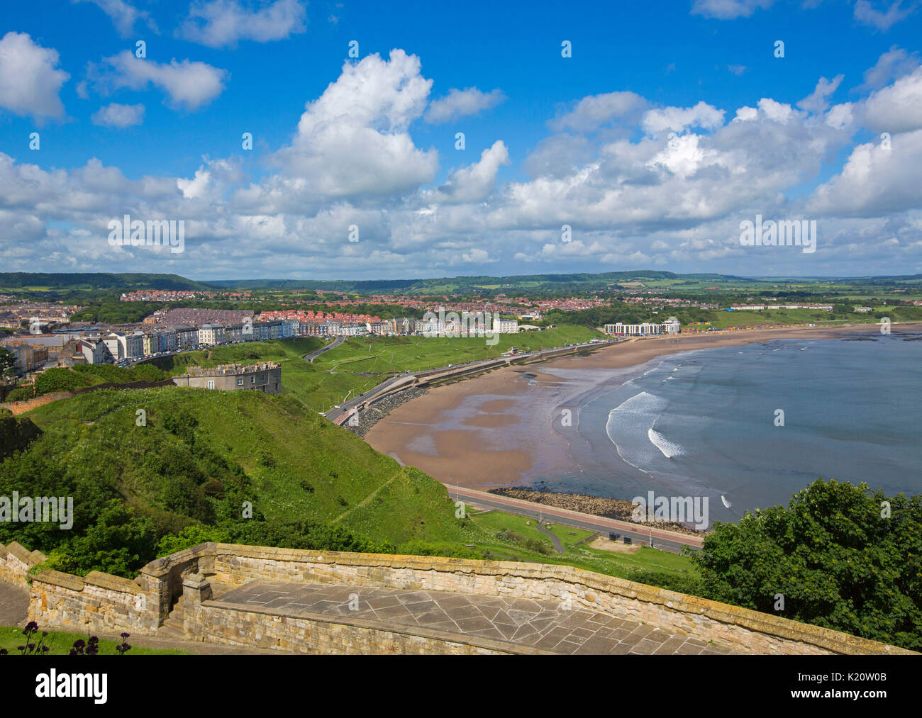 Tentacolare Città di Scarborough con spiaggia adiacente, porto, oceano e colline boscose sotto il cielo blu, visto dal castello storico nello Yorkshire Inghilterra Foto Stock