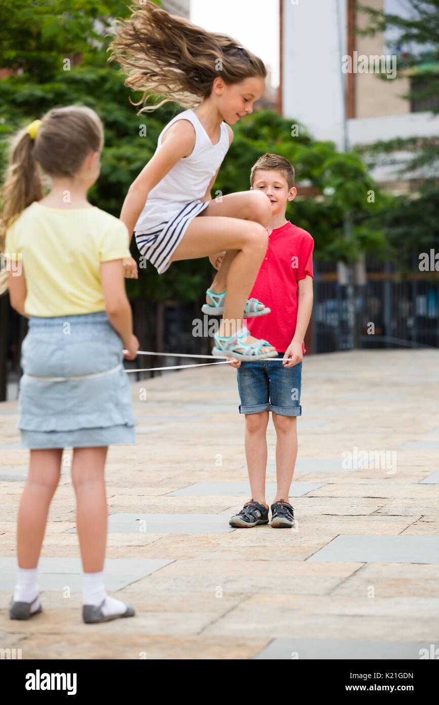Ragazzo allegro e le ragazze nella scuola elementare età divertendosi con il cinese salto con la corda . Messa a fuoco selettiva su boy Foto Stock