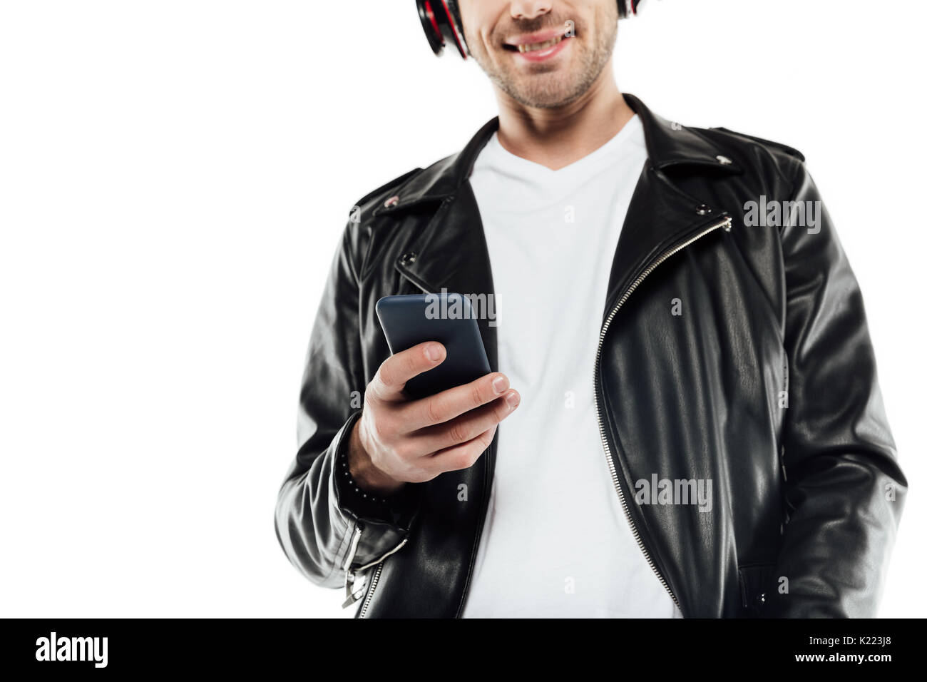 Giovane uomo in giacca di pelle ascoltando musica in cuffia mentre si utilizza lo smartphone Foto Stock