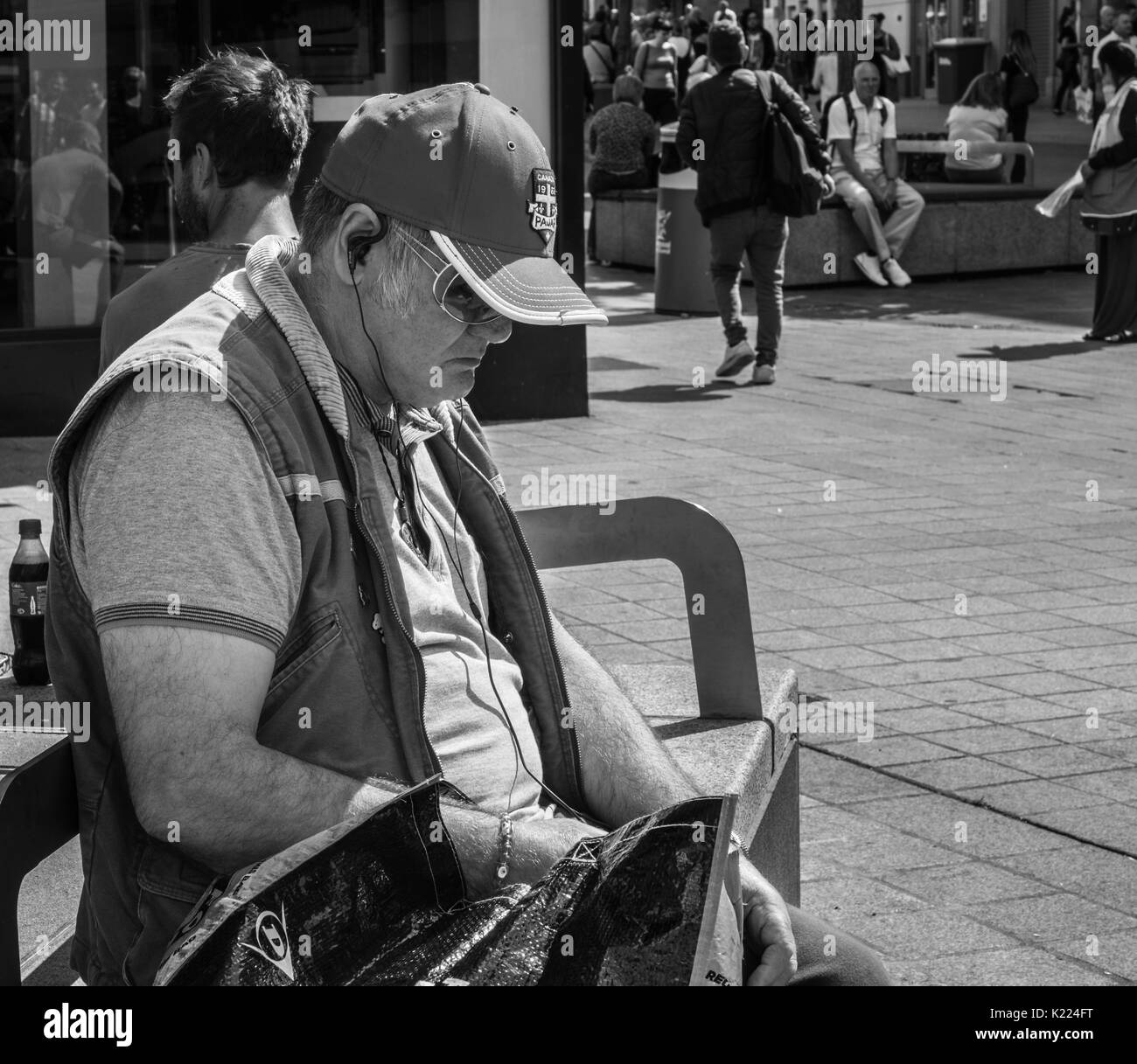 Uomo seduto su un banco di lavoro con gli auricolari e ascoltare musica. Liverpool, in Inghilterra, Regno Unito Foto Stock