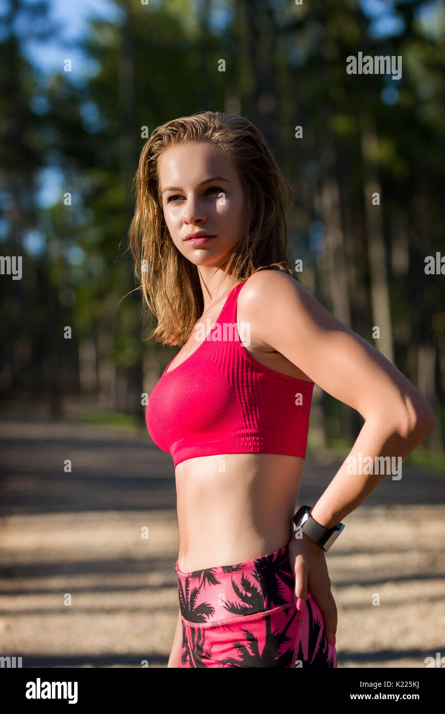 Montare attraente athletic donna in piedi in una foresta, sudorazione e prendendo una pausa da un intenso allenamento. Foto Stock