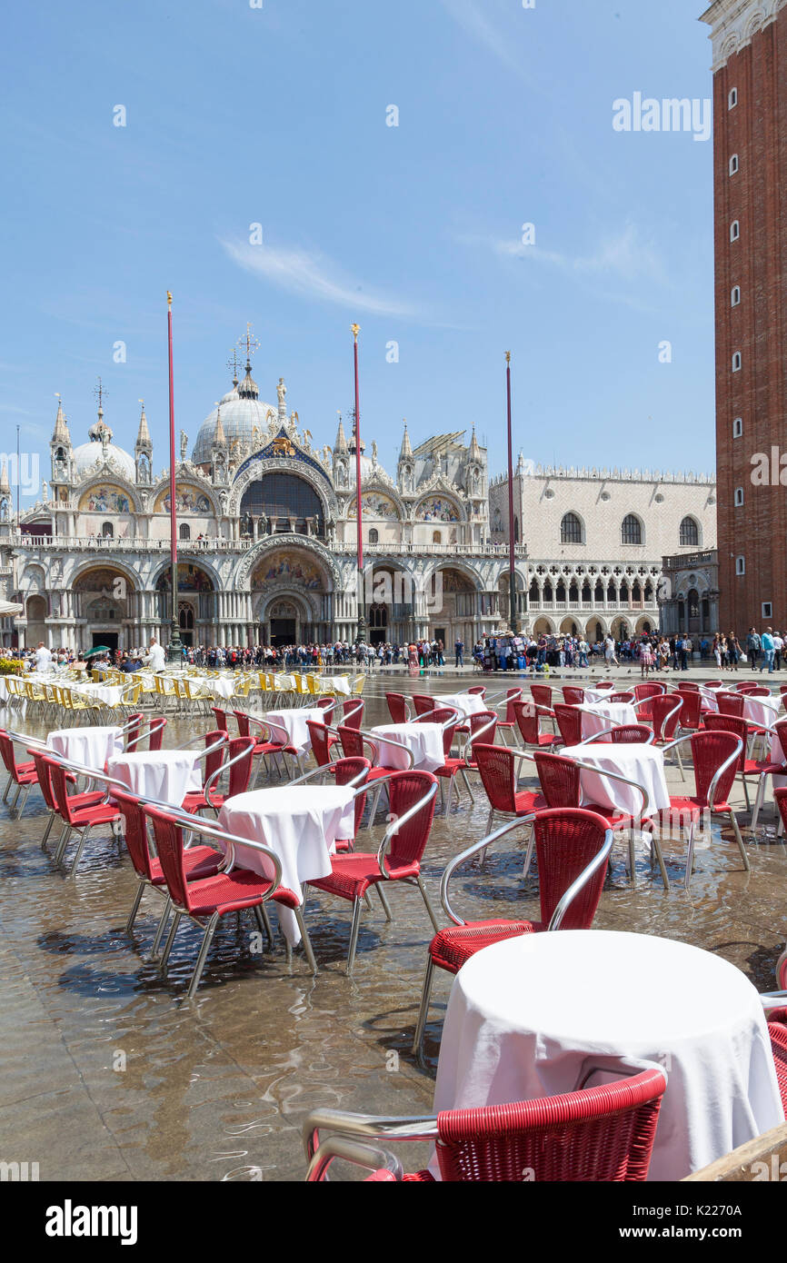 Acqua alta inondazioni in Piazza San Marco a mezzogiorno Venezia, Italia con acqua vorticoso vuoto arounf tavole di ristorante a mezzogiorno in una giornata di sole, Crow Foto Stock