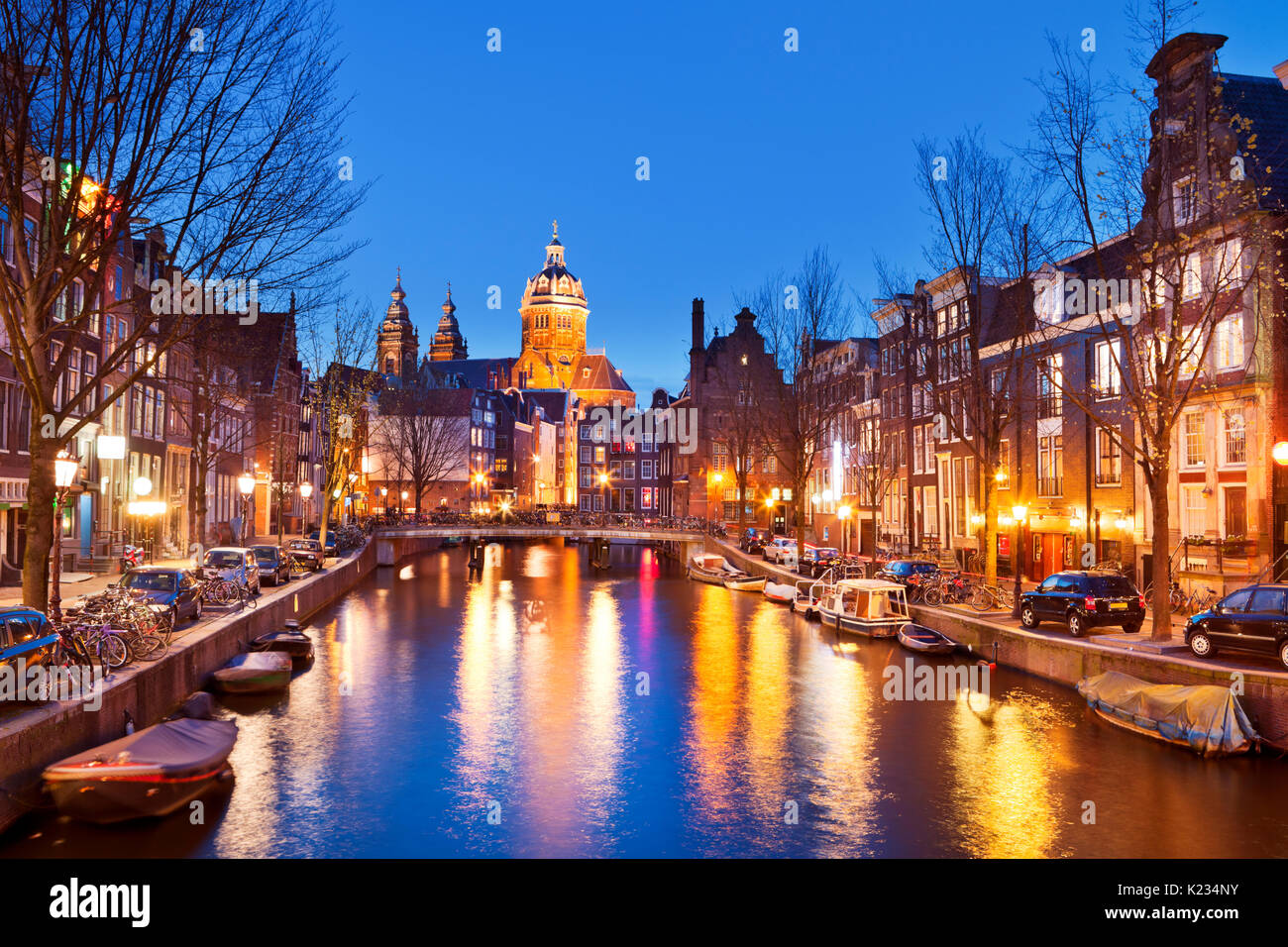Un canale nel quartiere a luci rosse di Amsterdam, Paesi Bassi con la chiesa di San Nicola alla fine. Fotografato di notte. Foto Stock