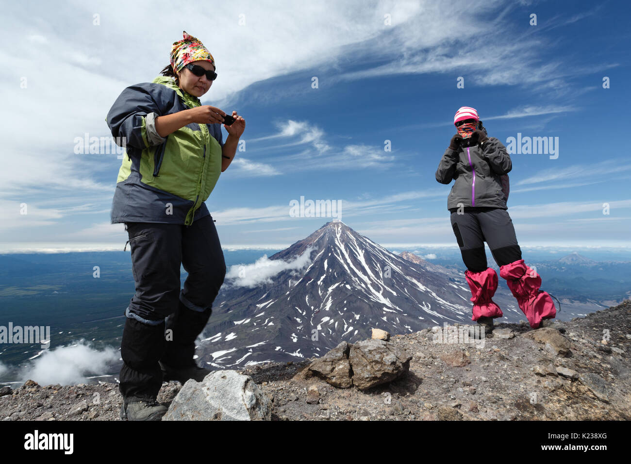 Escursioni in montagna - due donne giovani turisti stand della cima del cratere sommitale del attivo vulcano Avachinsky sullo sfondo del cono del vulcano popolare Koryak Foto Stock