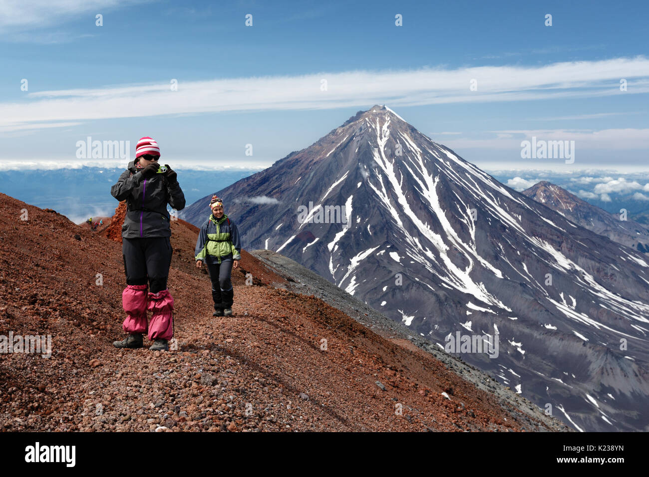 Due giovani donne i turisti sono a piedi lungo un percorso escursionistico di montagna sul bordo del cratere del vulcano attivo, fotografando paesaggio vulcanico su Kamchatka. Foto Stock