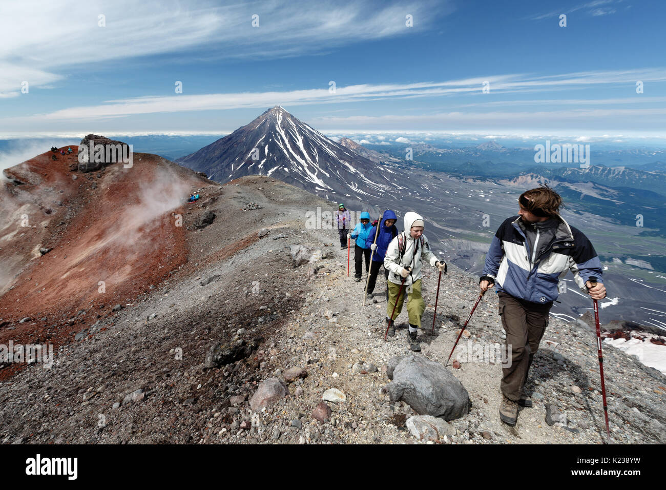 Gruppo di escursionisti che sale lungo il bordo del cratere sommitale del attivo vulcano Avachinsky sullo sfondo del cono del vulcano popolare Koryak sulla penisola di Kamchatka. Foto Stock