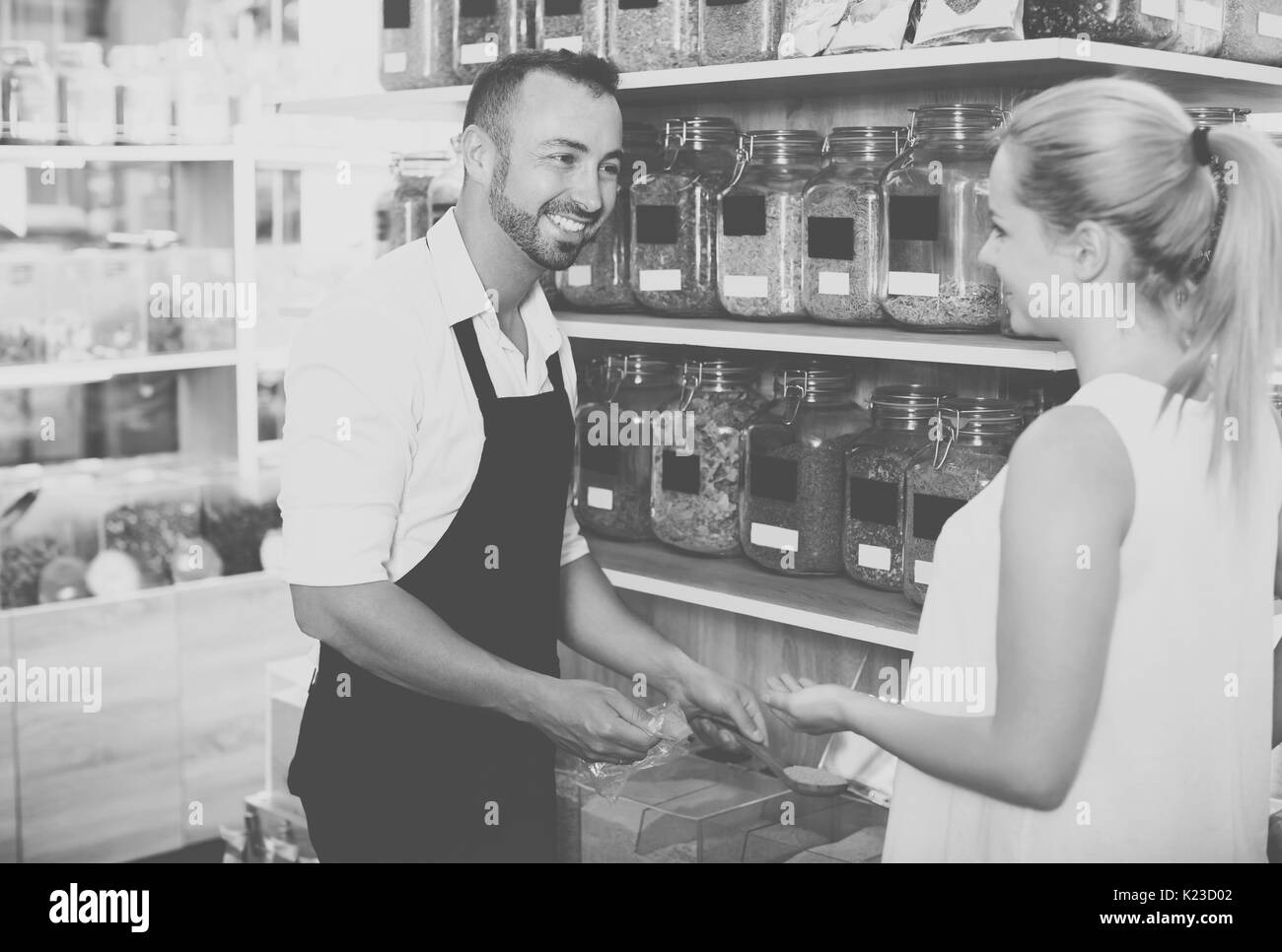 Uomo adulto venditore indossando il grembiule in piedi con i cereali venduti a peso in organico negozio Foto Stock