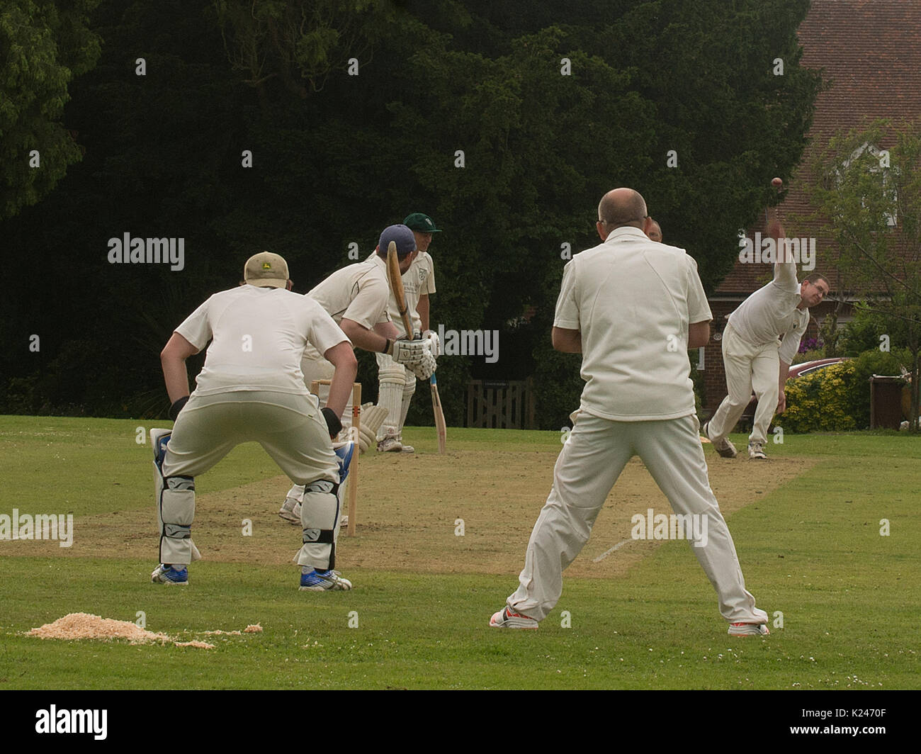 Vicino vista villaggio cricket partita sul verde villaggio a Benenden nel Kent con battitore, wicket custode e vicino anziani e palla lasciando mano di pugile Foto Stock