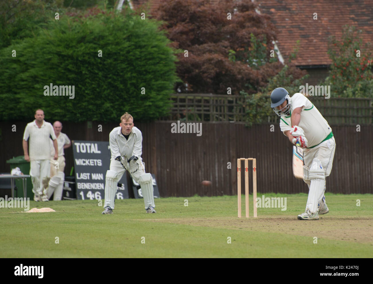 Battitore gioca un colpo in avanti in una partita di cricket villaggio con il portiere in posa classica e palla chiaramente visto Foto Stock