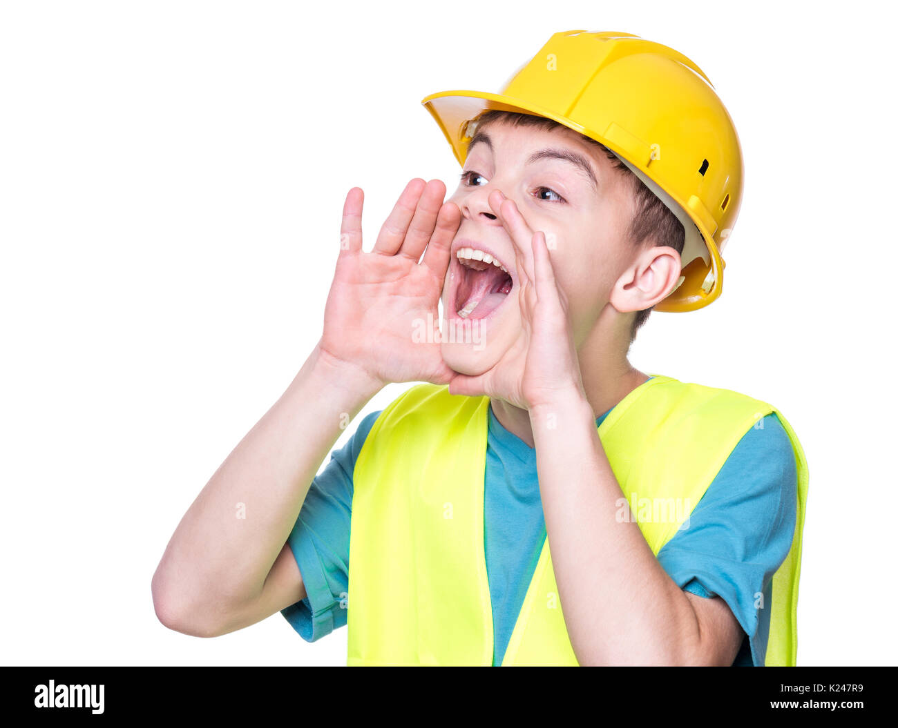 Ritratto emotivo del bello caucasian teen boy indossando giacca di sicurezza e casco giallo. Bambino felice urlando e guardando lontano, isolato su bianco Foto Stock