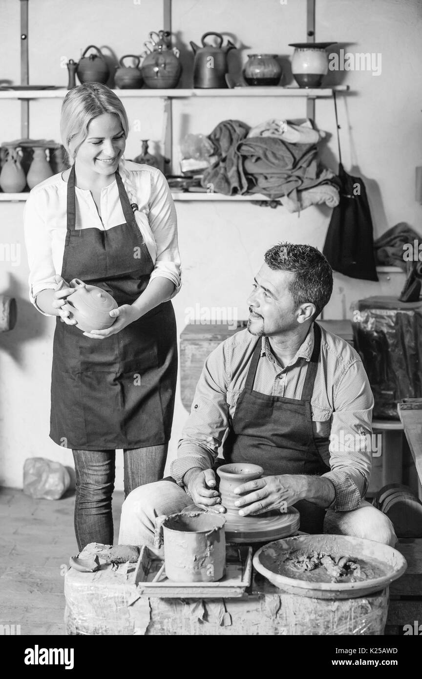 Sorridente artigiano rendendo pot con ruota in ceramica e a parlare con una donna collega in ceramica studio Foto Stock