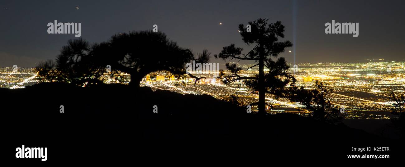 Il sole scende oltre le formazioni rocciose presso il Red Rock Canyon National Conservation Area con stagliano pinyon alberi di pino e dalle luci di Las Vegas nella distanza 26 Settembre 2016 vicino a Las Vegas, Nevada. Foto Stock