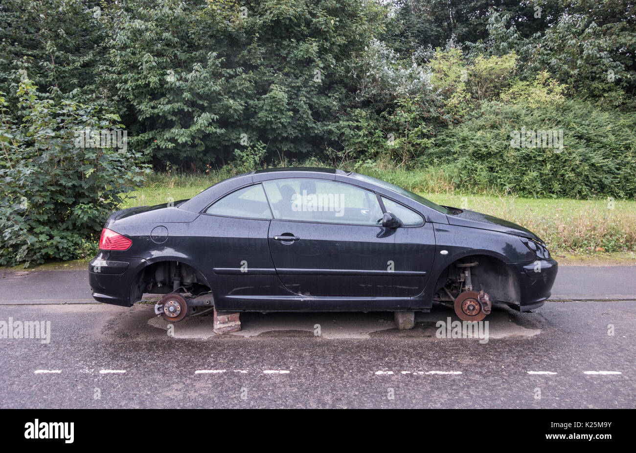 Auto con ruote rubato sollevato su mattoni in strada nel Regno Unito Foto Stock
