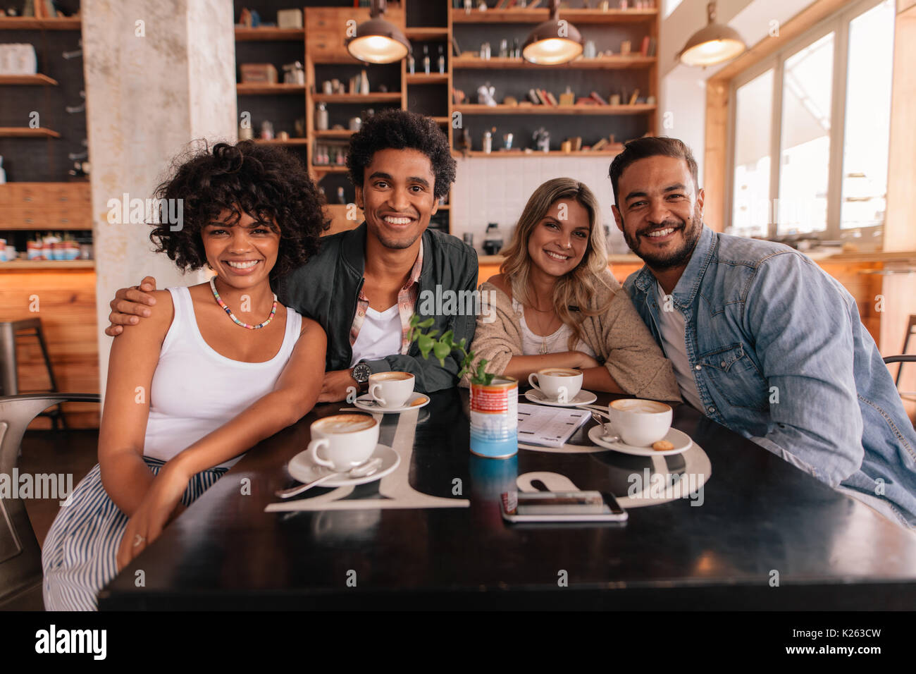 Ritratto di gruppo di amici seduti insieme in una caffetteria. I giovani riuniti in un caffè guardando la fotocamera e sorridente. Foto Stock