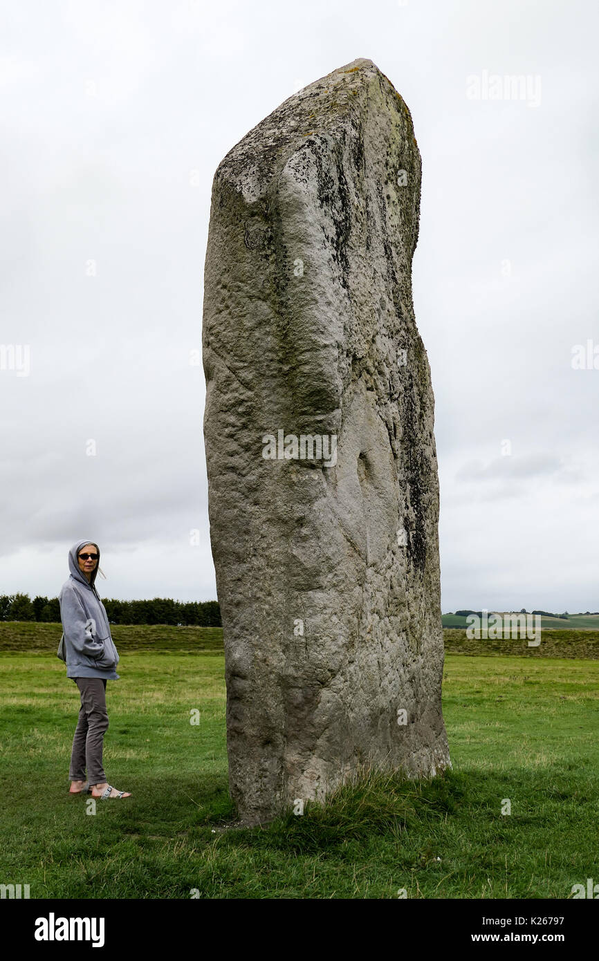 Una donna accanto alla pietra permanente ad Avebury, Wiltshire, Regno Unito Foto Stock