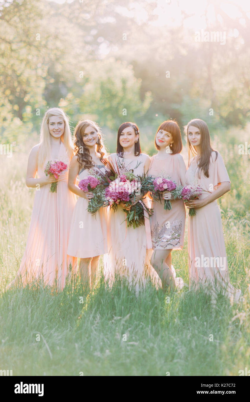 La foto di gruppo della sposa e le sue damigelle hanno premuto il enormi mazzi di fiori di colore rosa nel centro del soleggiato verde foresta. Foto Stock