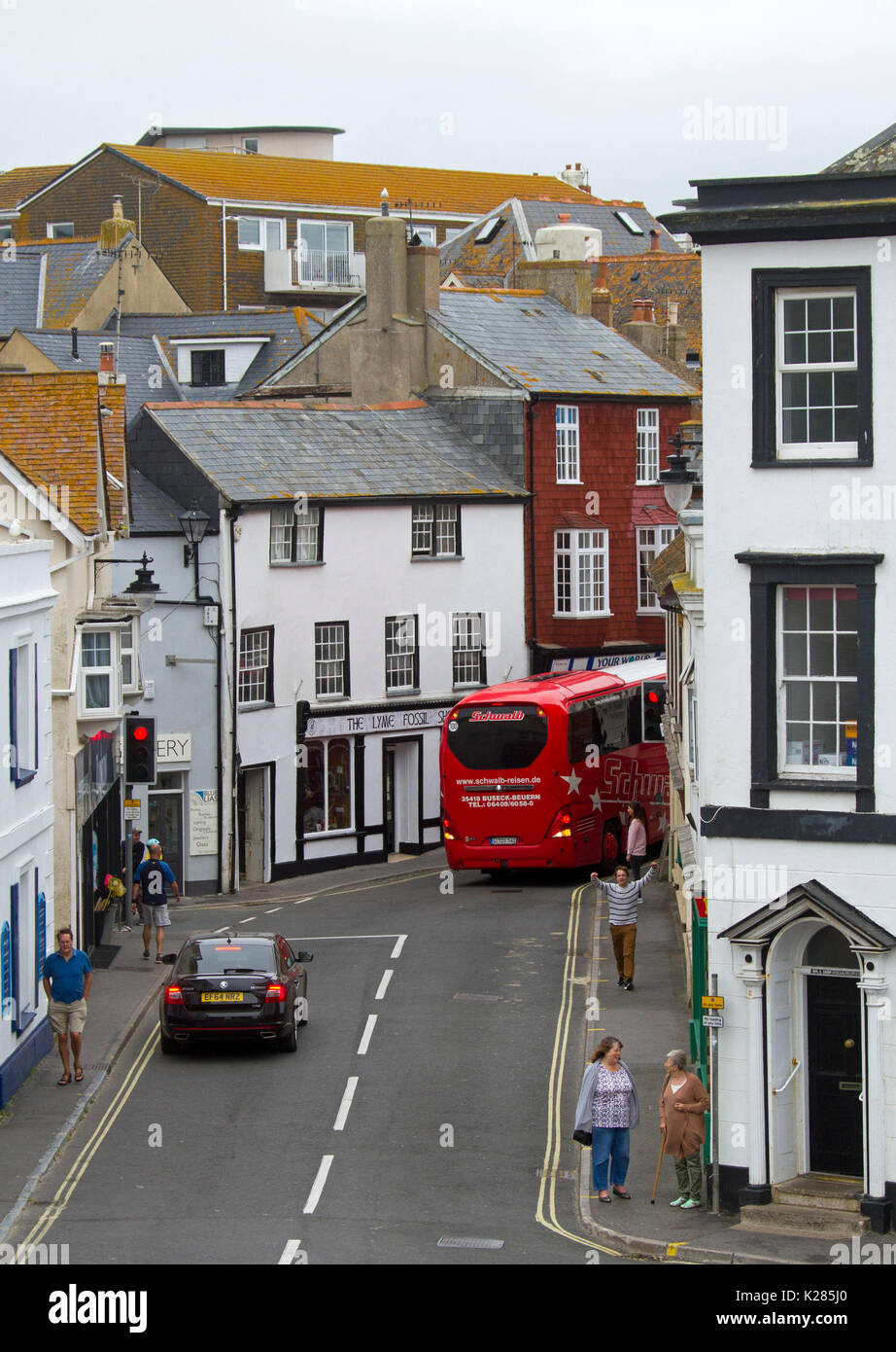 Pullman turistico, auto e pedoni in strada stretta tra alti edifici di Lyme Regis, West Dorset, Inghilterra Foto Stock