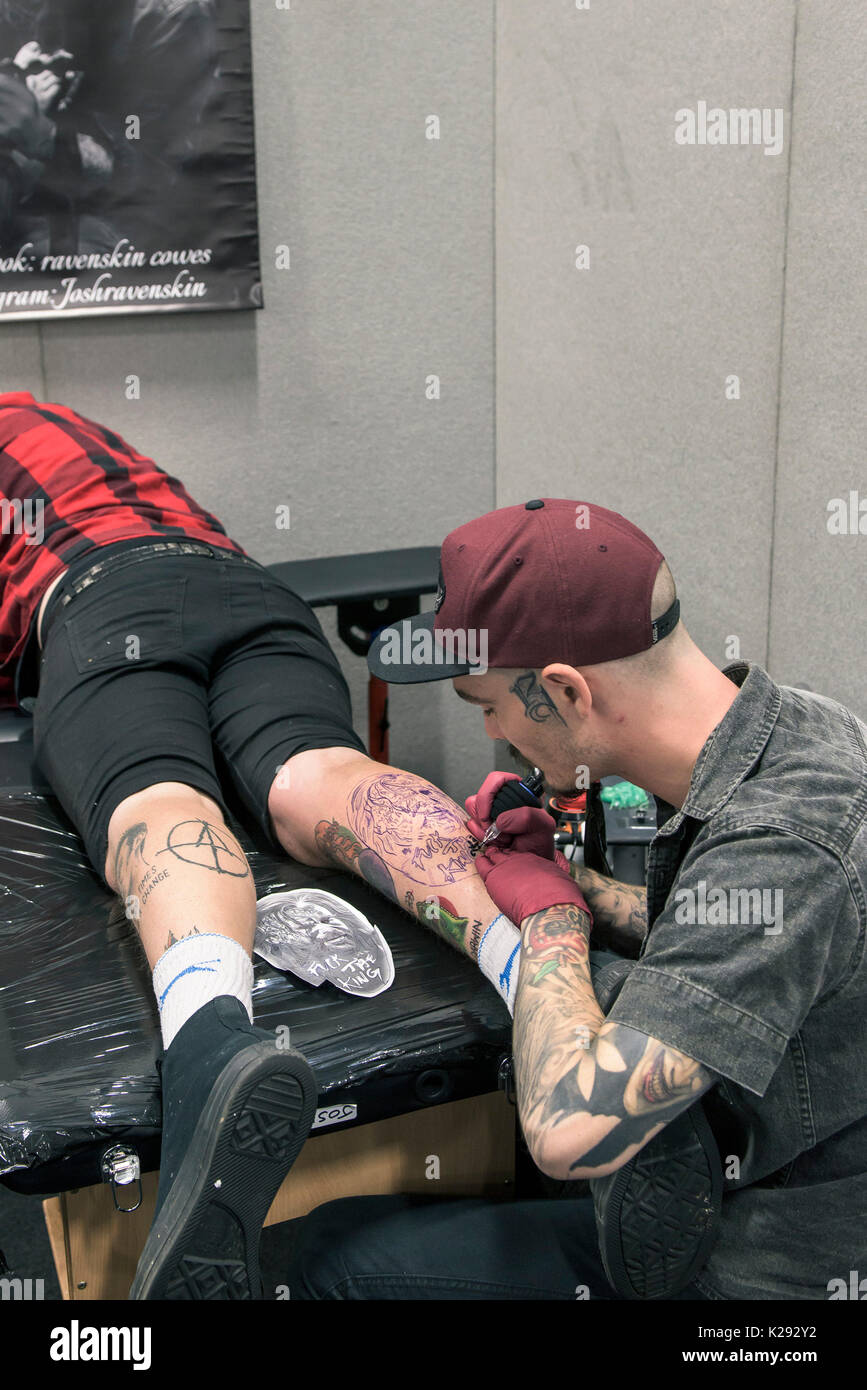 Tatuaggio - Josh Docksey tatuaggio la gamba di un cliente al Cornwall Tattoo Convention. Foto Stock