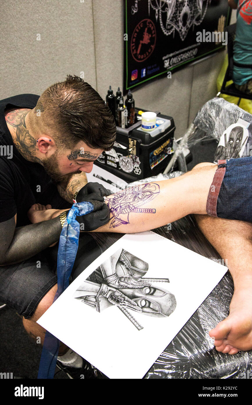 Tatuaggio - Luca Rudden tatuaggio un disegno sulla gamba di un cliente fmale a Cornwall Tattoo Convention. Foto Stock