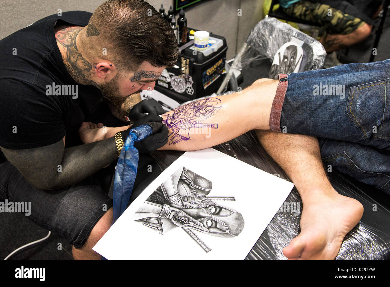 Cornovaglia Tattoo Convention - Luca Rudden tatuaggio un disegno sulla gamba di un cliente fmale a Cornwall Tattoo Convention. Foto Stock