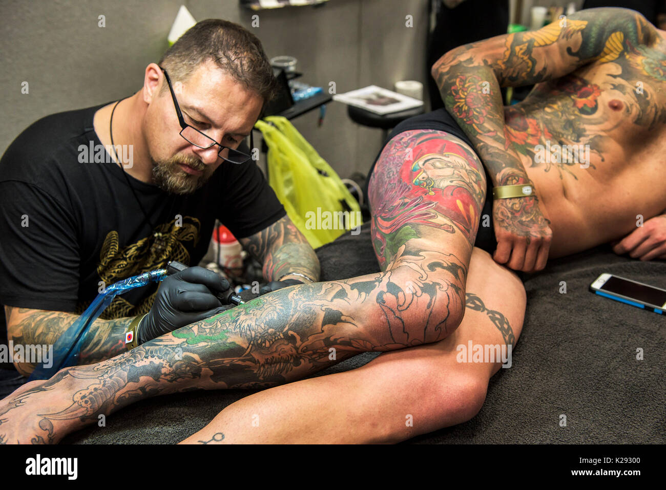 Tatuaggio - Luca Botterill tatuaggio un disegno sulla gamba di un cliente al Cornwall Tattoo Convention. Foto Stock