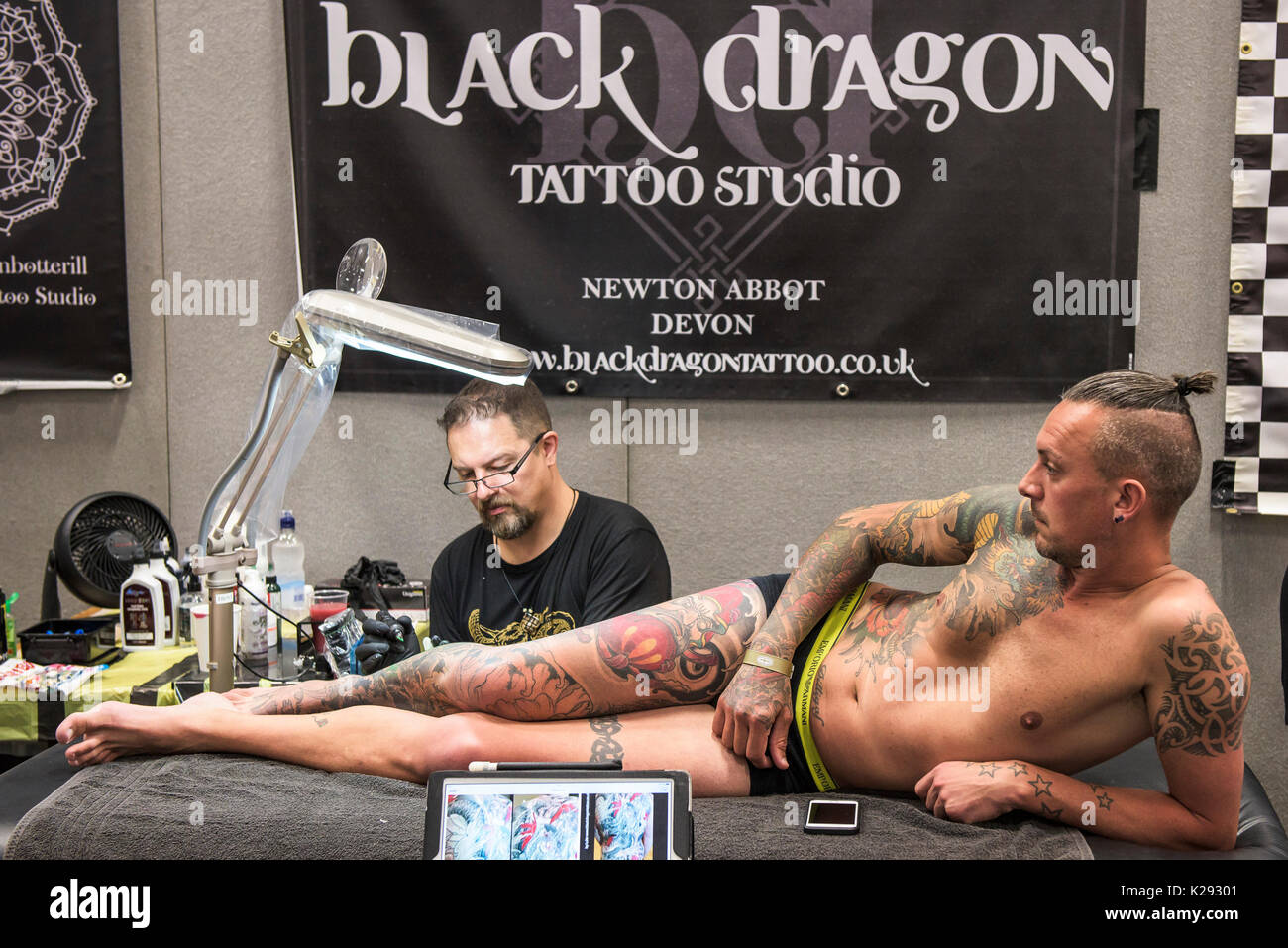 Tattoo - Luca Botterill tatuaggio un disegno sulla gamba di un cliente al Cornwall Tattoo Convention. Foto Stock