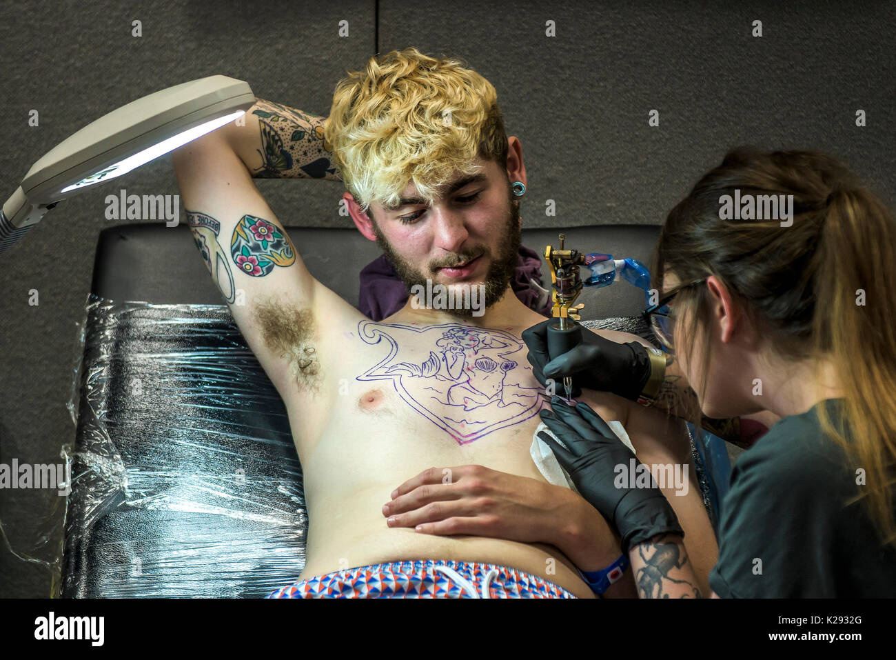 Tattoo - Femmina tattooist Angelo pazzo tatuaggio un disegno sul petto di un cliente al Cornwall Tattoo Convention. Foto Stock