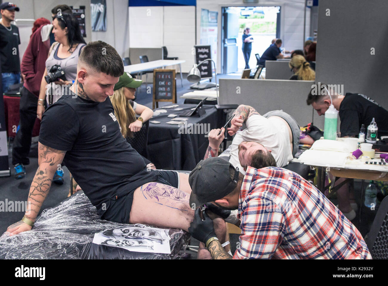 Cornovaglia Tattoo Convention - un cliente a guardare la sua coscia essendo tatuati in Cornovaglia Tattoo Convention. Foto Stock