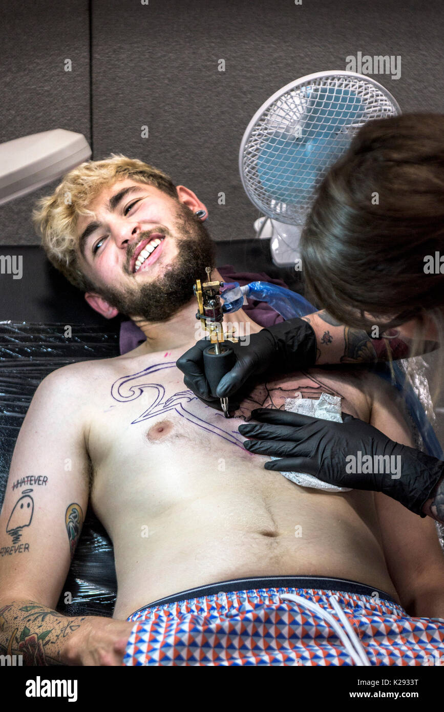 Cornovaglia Tattoo Convention - un cliente di fronte a dolore come tattooist tatuaggi un progetto sul suo petto in Cornovaglia Tattoo Convention. Foto Stock