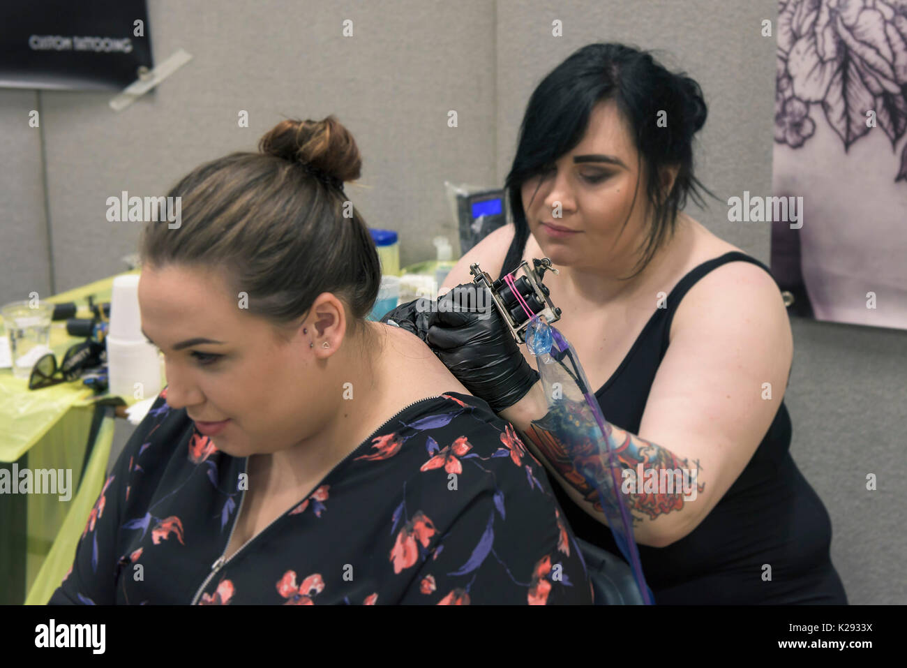 Cornovaglia Tattoo Convention - la femmina tattooist Laura G applicando un tatuaggio al retro di una femmina di cliente al Cornwall Tattoo Convention. Foto Stock