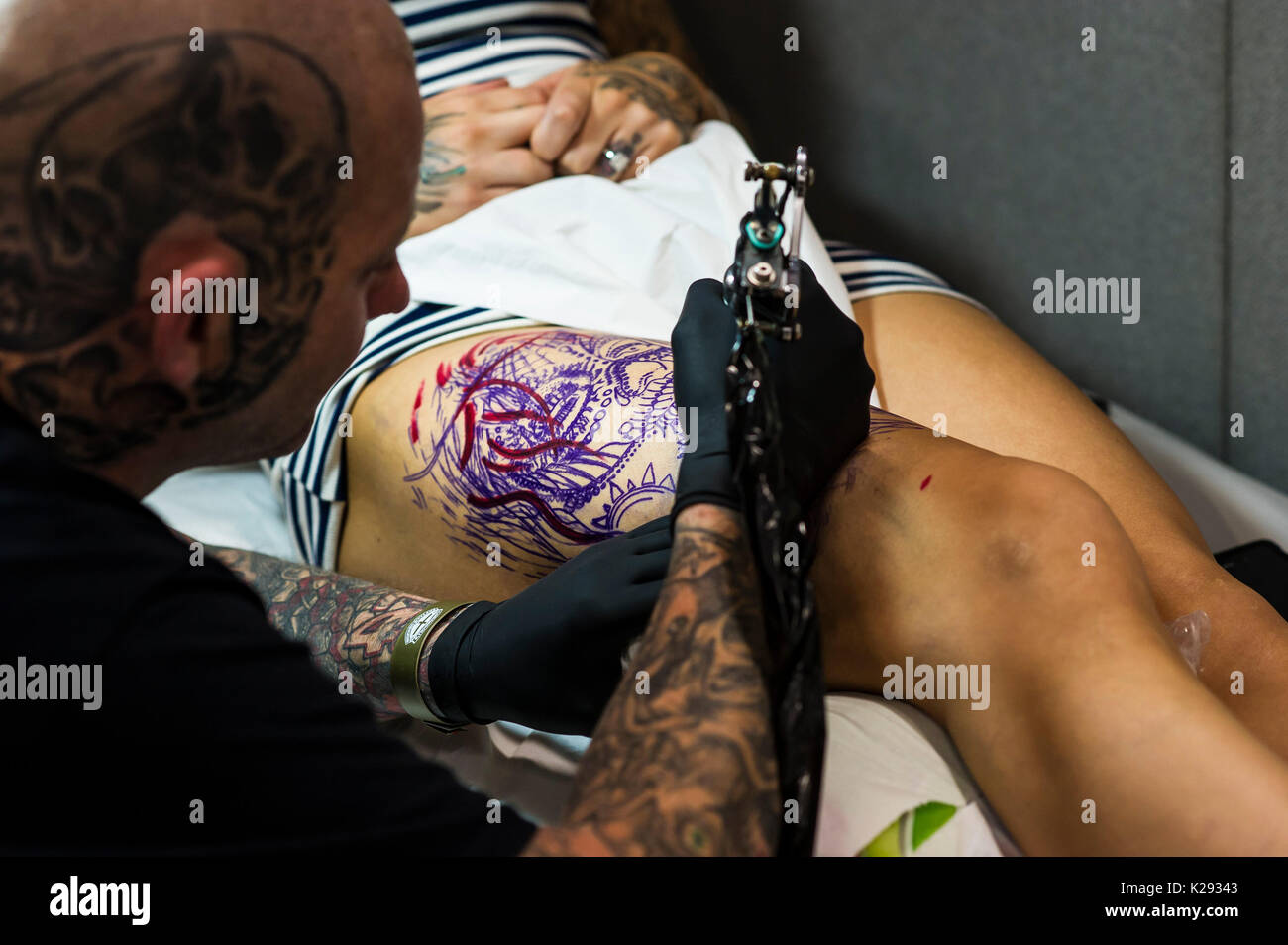 Cornovaglia Tattoo Convention - un tattooist lavorando su un progetto sulla coscia di un cliente al Cornwall Tattoo Conventiuon. Foto Stock